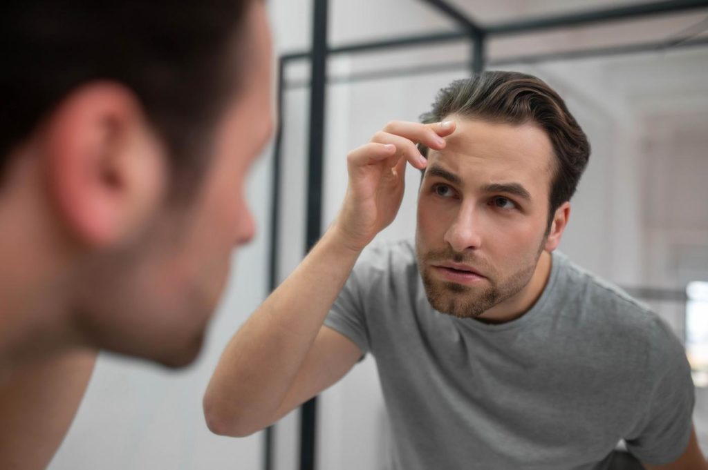 Hombre revisando en el espejo la caída de su pelo por estres